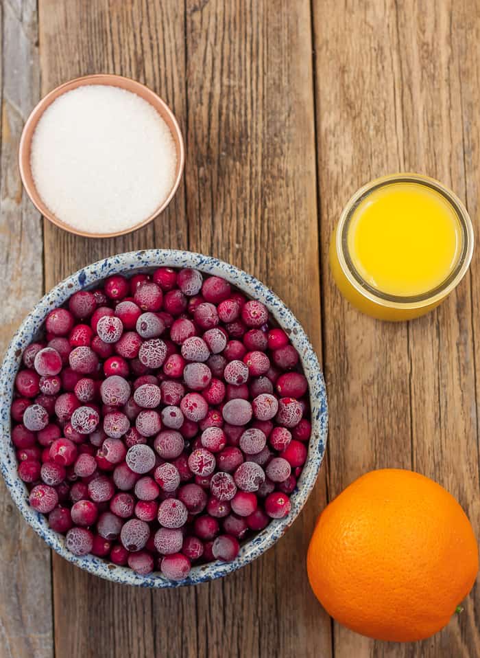 sugar, orange juice, an orange, and a bowl of cranberries.