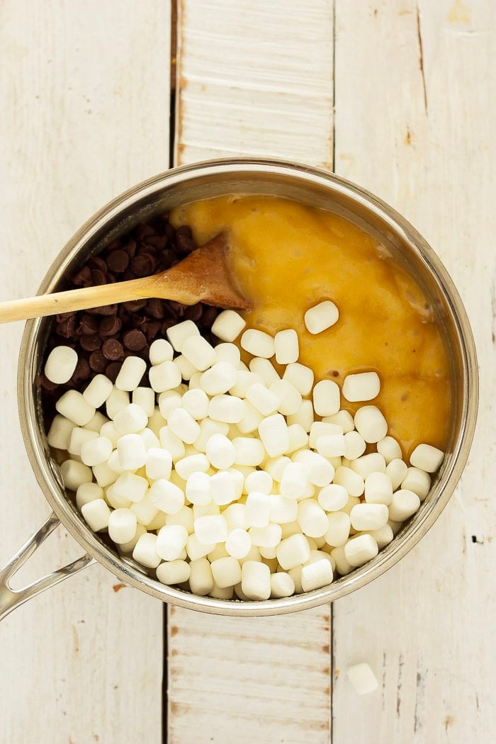 mini marshmallows, chocolate chips, and evaporated milk in a saucepan with a wooden spoon.