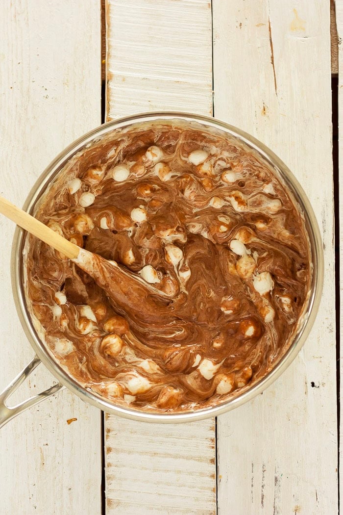 a wooden spoon mixing mini marshmallows into a mixture of chocolate.