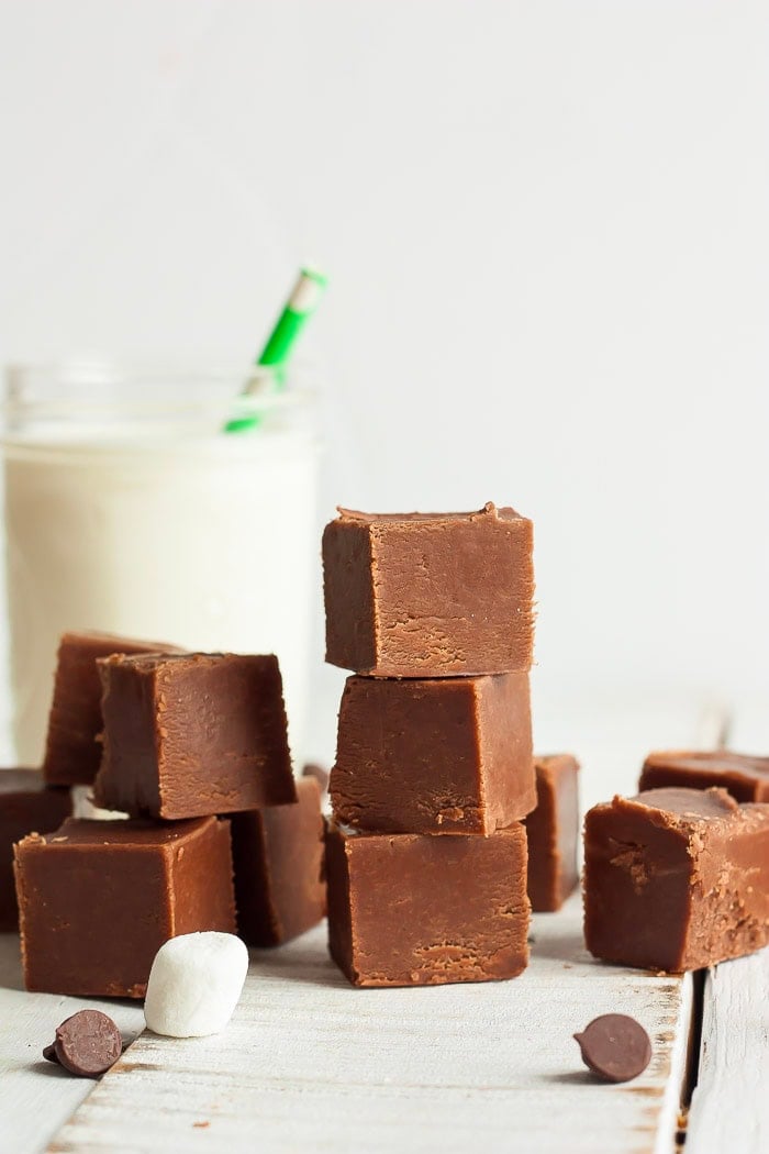 squares of fudge stacked on a white board with a canning jar of milk.