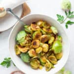 a white bowl of roasted honey sriracha brussel sprouts with a fork on a white board