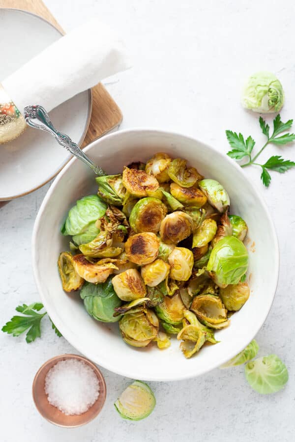 a white bowl of roasted honey sriracha brussel sprouts with a fork on a white board