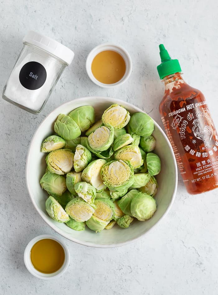 brussel sprouts, sriracha, honey, olive oil, and salt on a white board