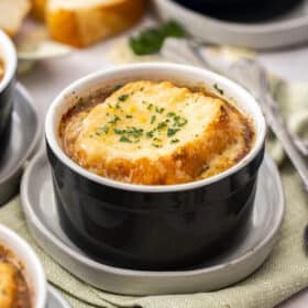 a small black ramekin with instant pot french onion soup topped with bread and melty cheese