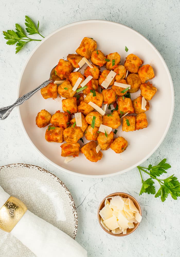 A white plate with gnocchi tossed with tomato sauce, parsley, and shredded Parmesan