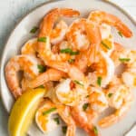 a plate of air fryer frozen shrimp with chopped parsley and a lemon wedge