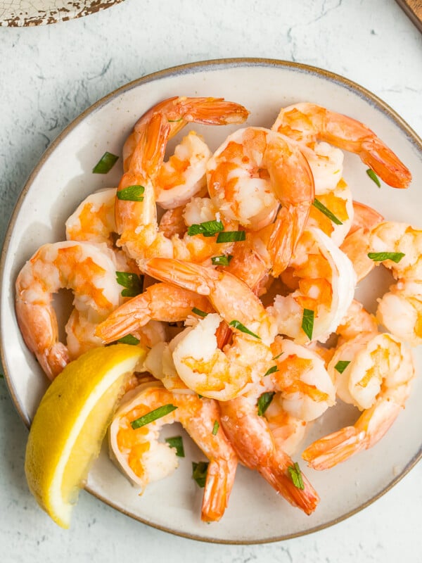 a plate of air fryer frozen shrimp with chopped parsley and a lemon wedge