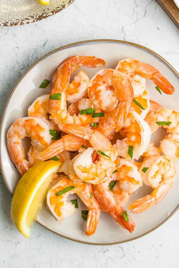 a plate of air fryer frozen shrimp with chopped parsley and a lemon wedge