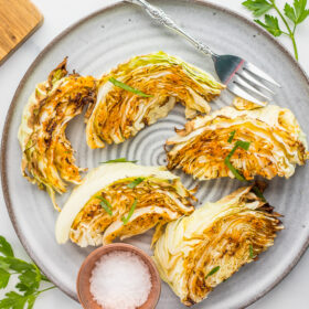 5 roasted cabbage wedges on a grey plate with a fork and a small bowl of kosher salt.