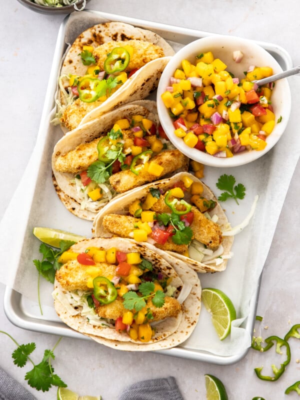 crispy air fryer fish tacos in tortillas on a tray with a bowl of mango salsa