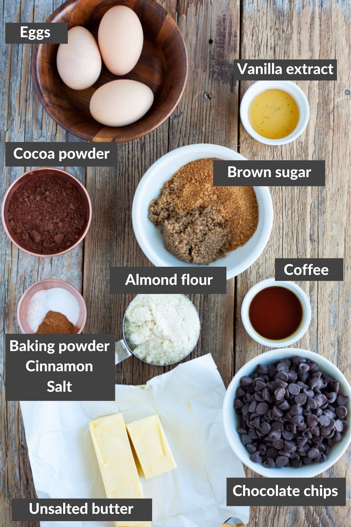 eggs, cocoa powder, sugar, vanilla extract, almond flour, and other ingredients on a wooden board.