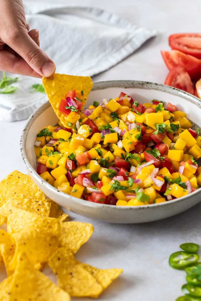 a hand scooping mango salsa with a chip