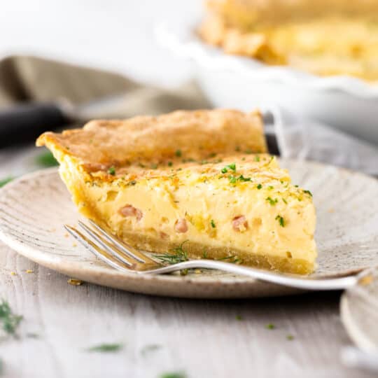 a slice of ham and swiss quiche on a grey plate with a fork.