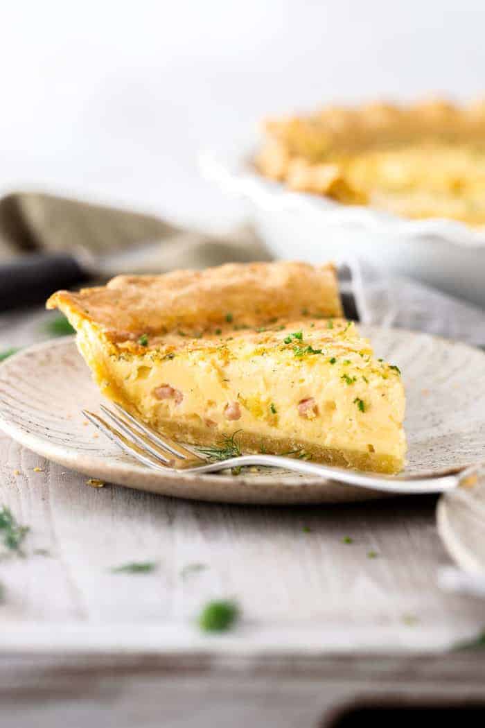 a slice of ham and swiss quiche on a grey plate with a fork.