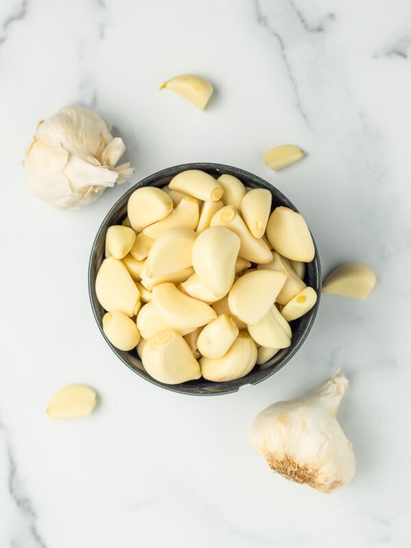 a dark blue bowl filled with cloves of garlic and 2 heads of garlic.