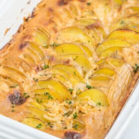 a white baking dish of gluten-free scalloped potatoes topped with thyme