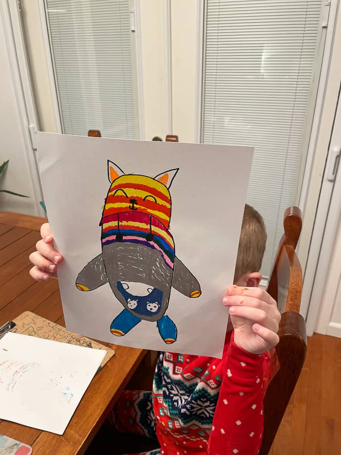 a child holding a colorful drawing of a kitten in a sweater.