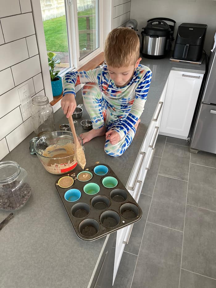 a kid on the counter filling muffin tins