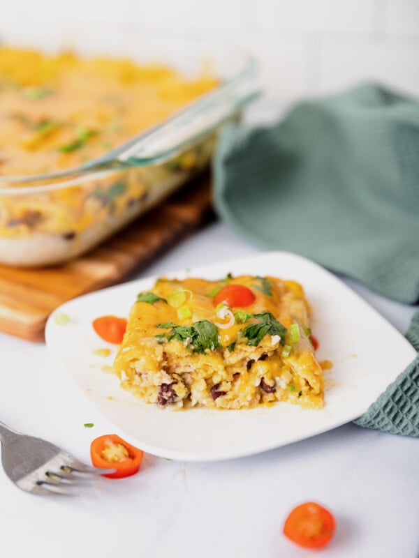 a white plate with a scoop of taquito casserole and tomatoes.