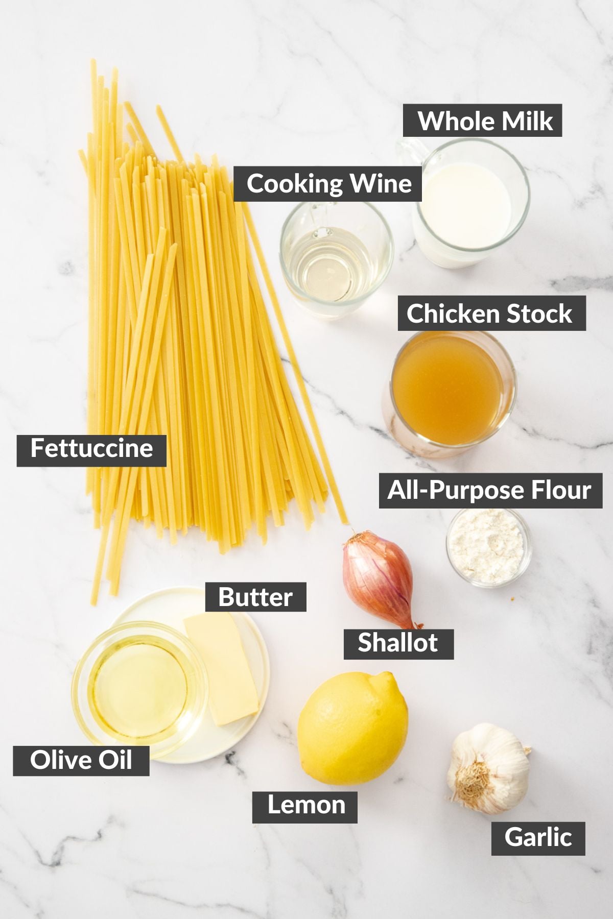 fettuccine, shallots, milk, a lemon, and other ingredients on a marbled board.
