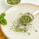 a measuring spoon with dried oregano on a dish.