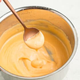 a spoon with gluten-free cheese sauce over a saucepan