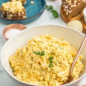 mayo free egg salad in a white bowl with brown bread and eggs on a white board