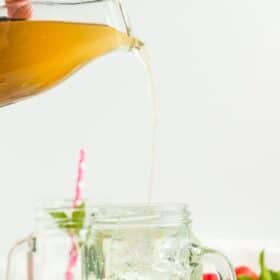 a small glass bottle pouring honey syrup into a glass with ice cubes and water