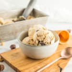 a grey bowl with peanut butter ice cream on a wooden board with a spoon.