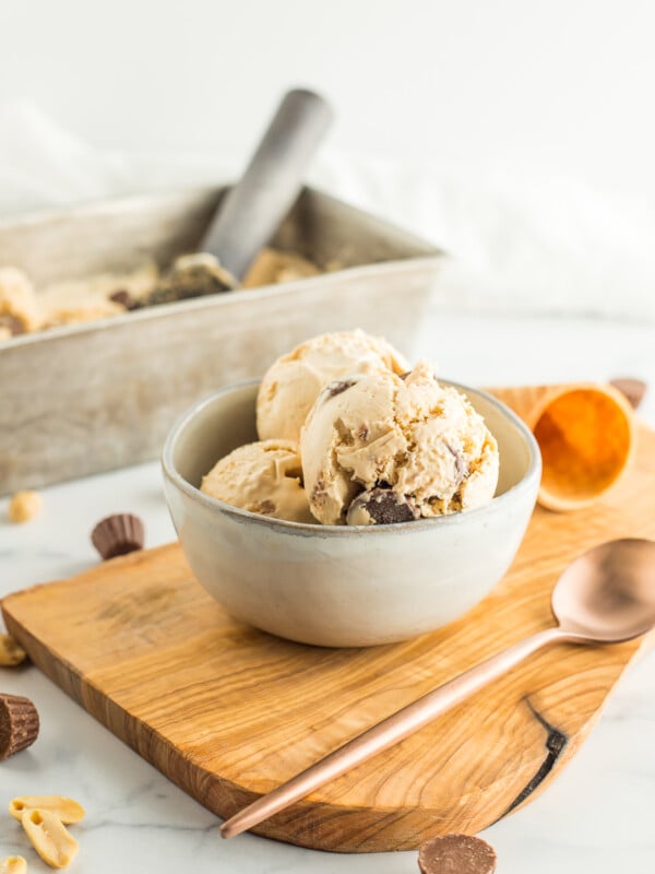 a grey bowl with peanut butter ice cream on a wooden board with a spoon.