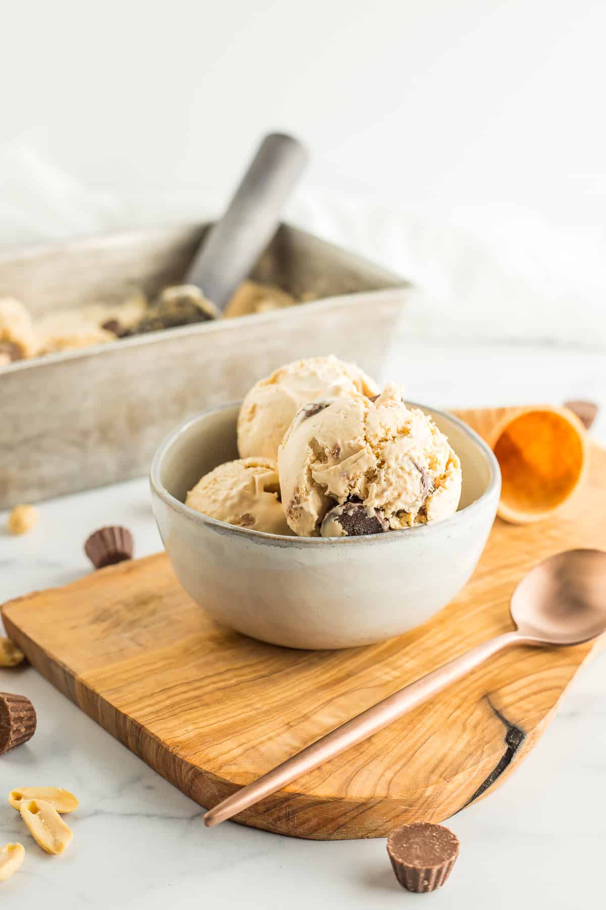 a grey bowl with peanut butter ice cream on a wooden board with a spoon.