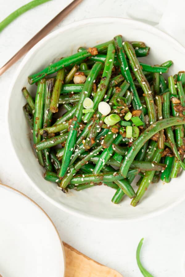 a white bowl with stir fried green beans and sliced green onions.