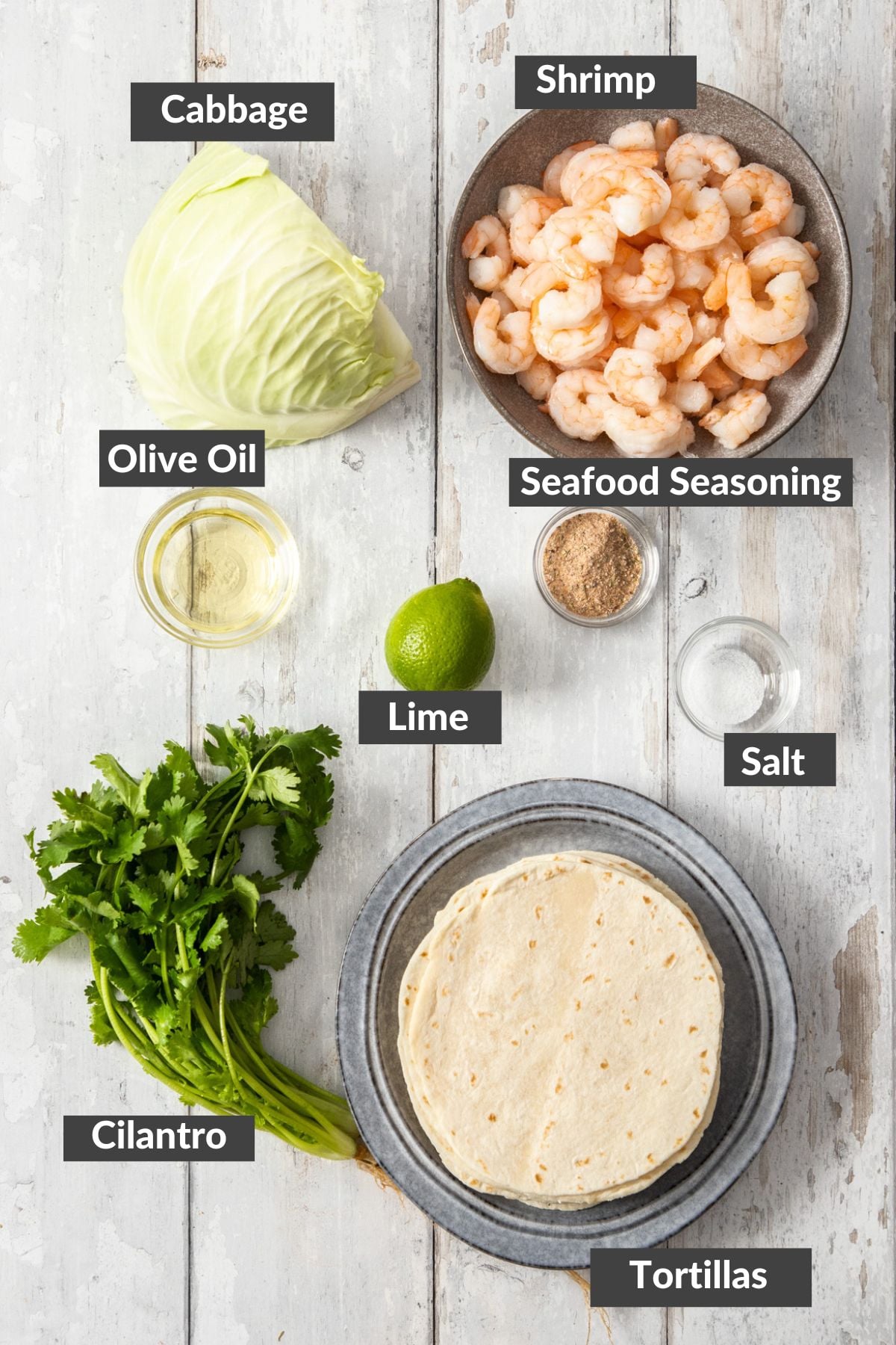 cabbage, tortillas, cilantro, lime, prawns, and other ingredients on a wooden board.