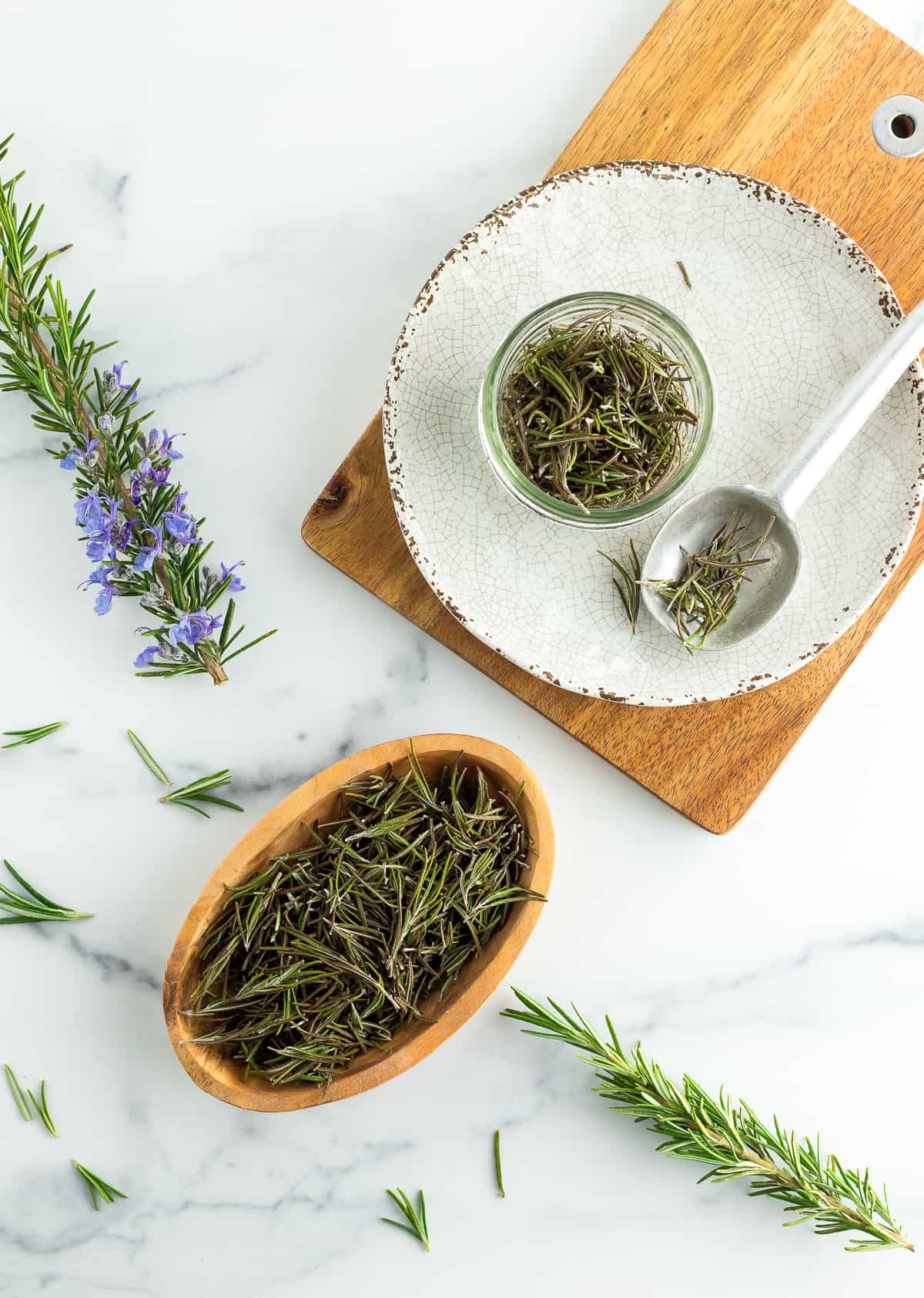 dried rosemary in a wooden bowl and on a beige plate with a spoon of rosemary.