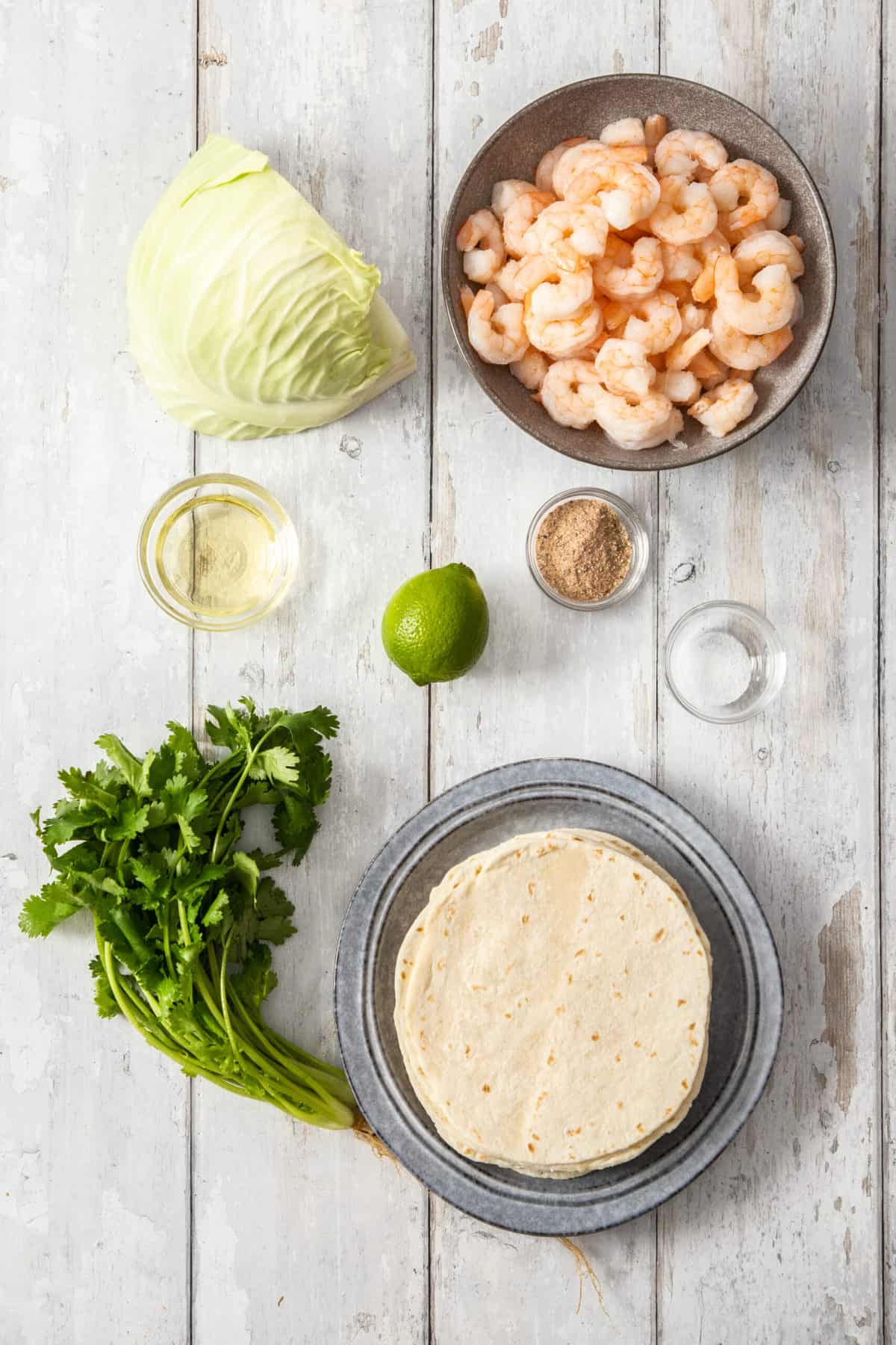 tortillas, shrimp, cabbage, and other ingredients on a wooden board.
