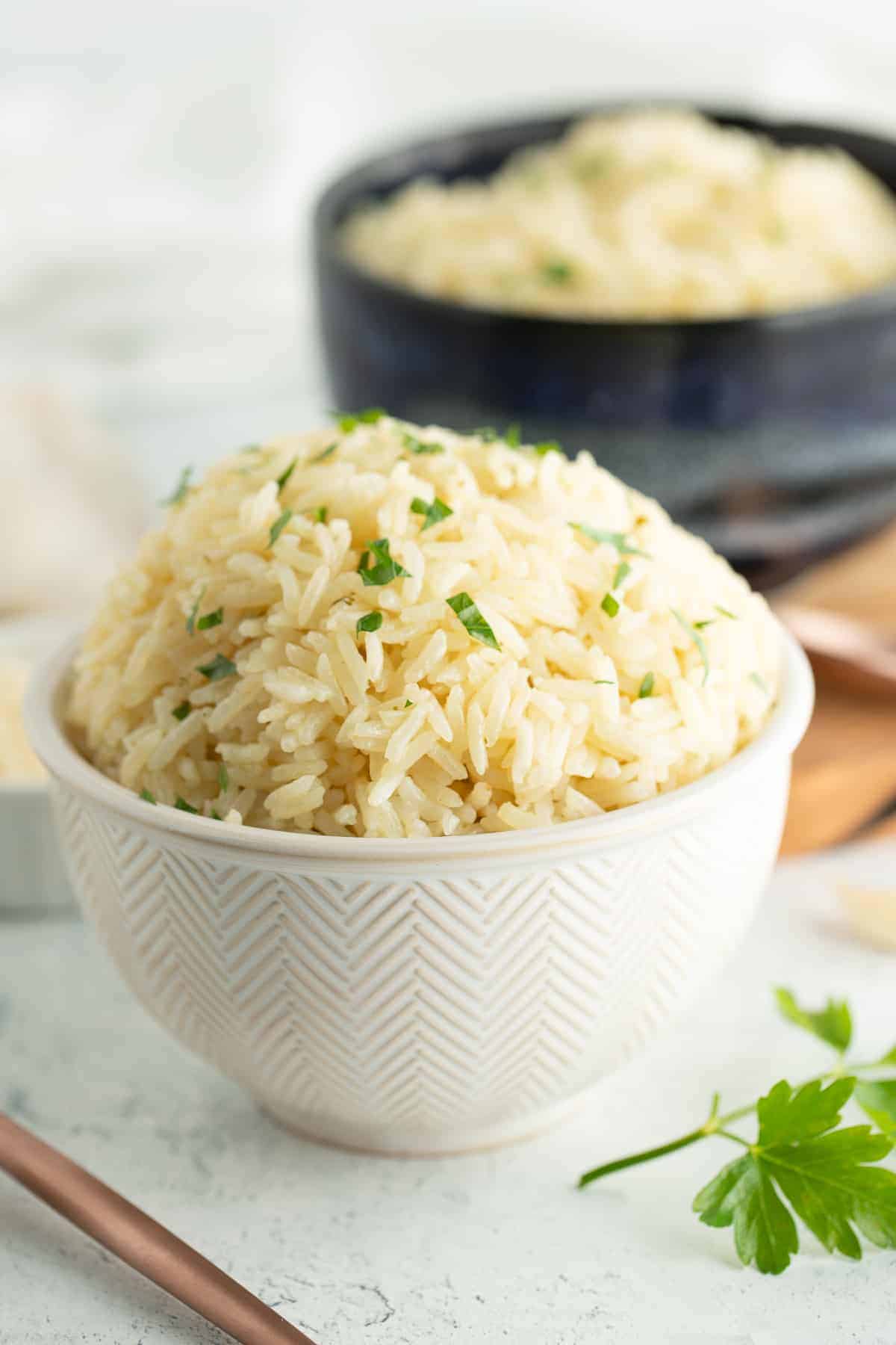 a white and blue bowl with garlic rice topped with chopped parsley.