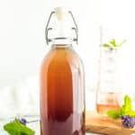 a bottle of lavender syrup in front of a glass of sparkling water with mint.