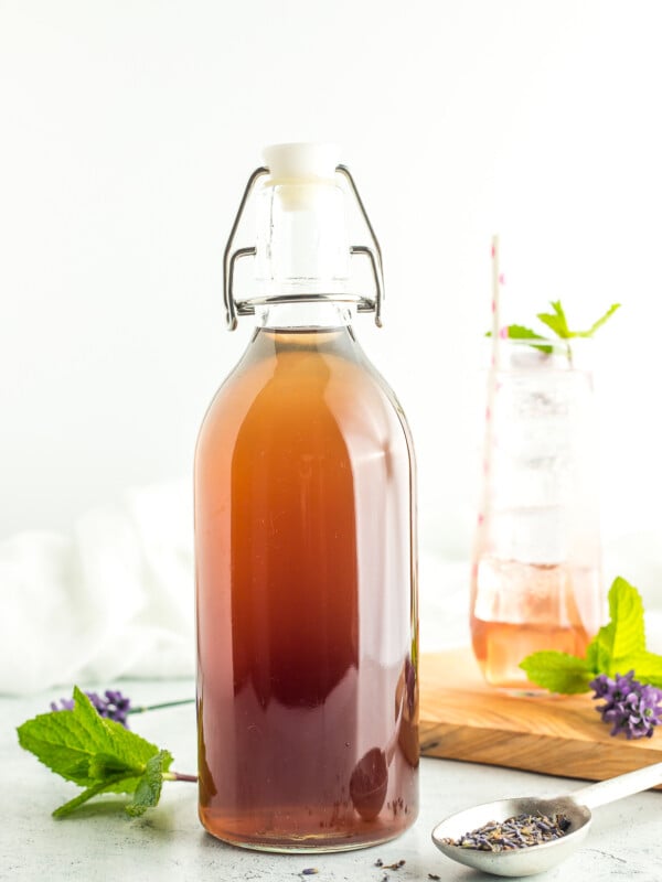 a bottle of lavender syrup in front of a glass of sparkling water with mint.