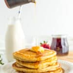 a stack of oatmilk pancakes on a plate with syrup being poured over it.