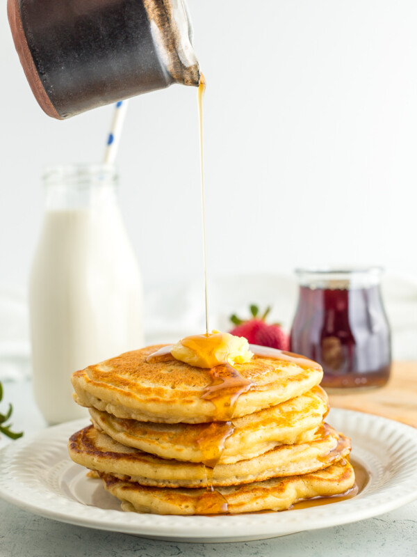 a stack of oatmilk pancakes on a plate with syrup being poured over it.