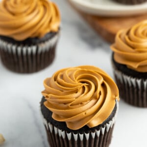 4 chocolate cupcakes with peanut butter cream cheese frosting on a white board.