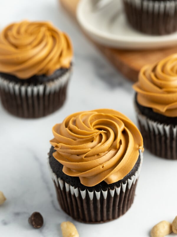 4 chocolate cupcakes with peanut butter cream cheese frosting on a white board.