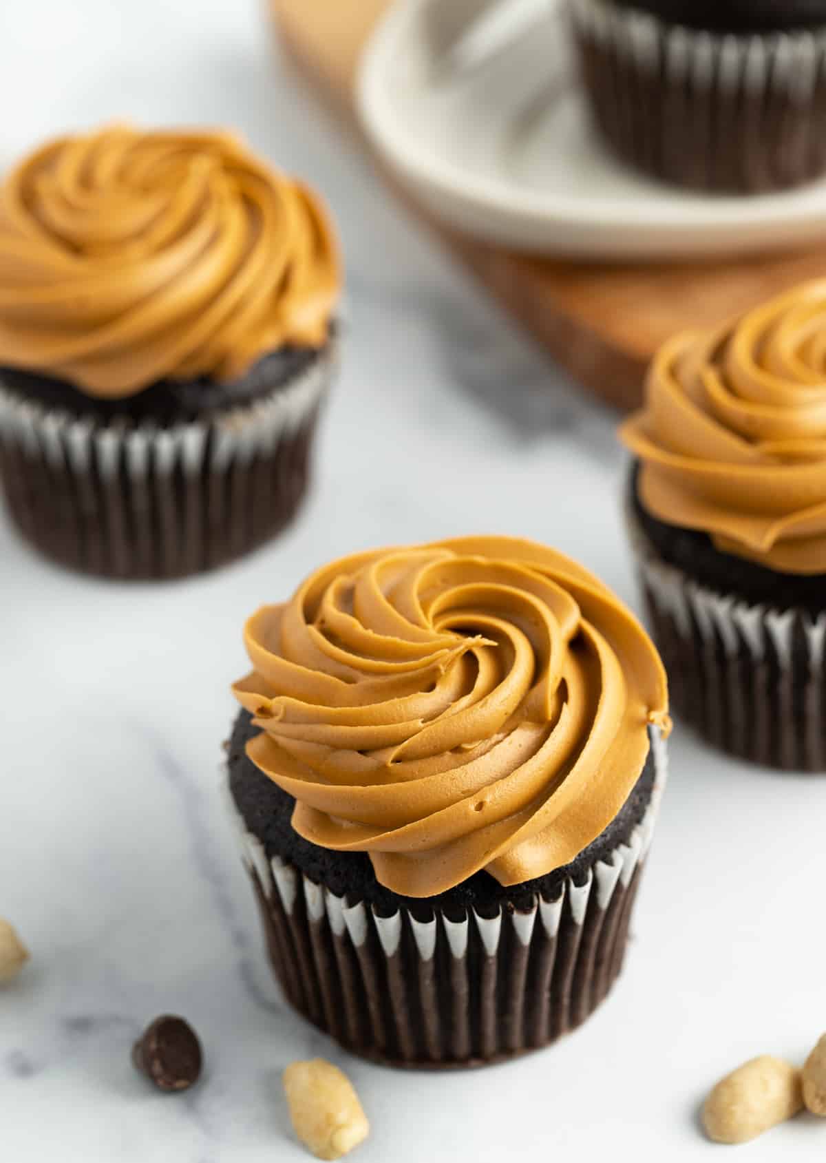 4 chocolate cupcakes with peanut butter cream cheese frosting on a white board.