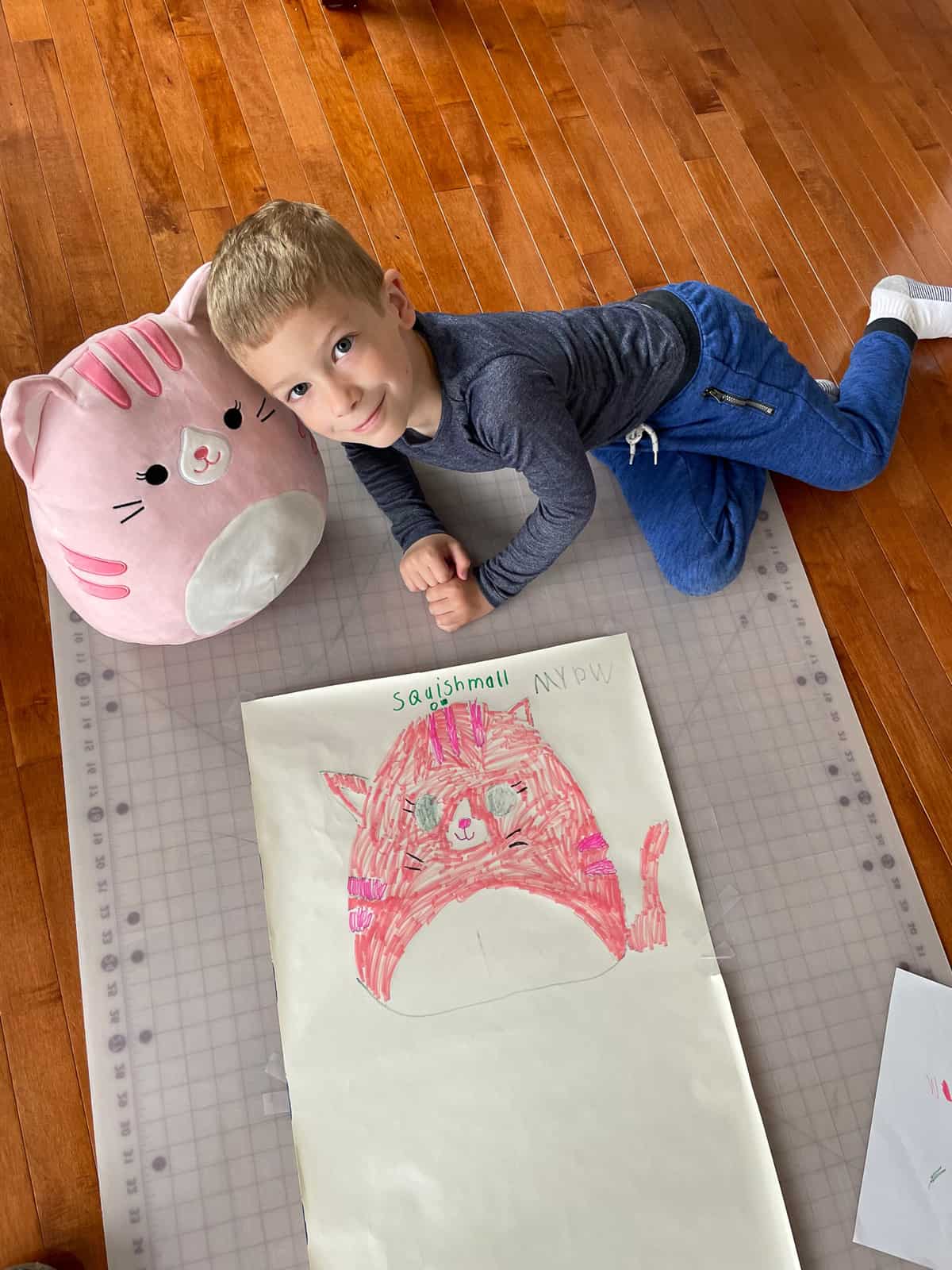 a kid with a stuffed animal and a picture he drew of it.