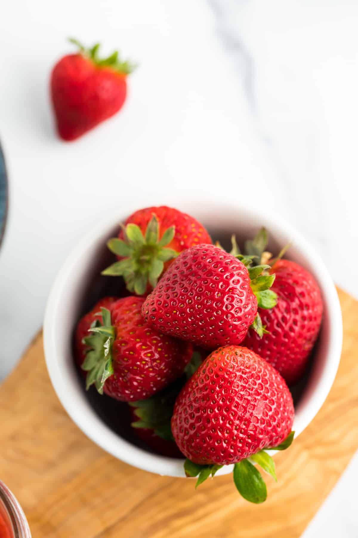 a bowl of strawberries on a white and wooden board