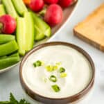 a grey bowl with vegan aioli topped with sliced green onions with a plate of vegetables.