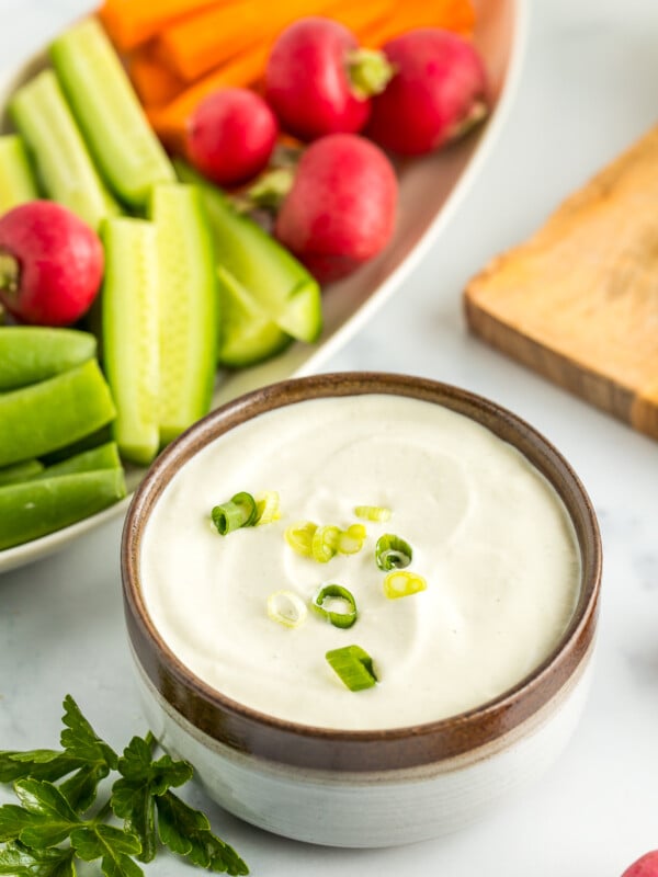 a grey bowl with vegan aioli topped with sliced green onions with a plate of vegetables.