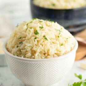 a white and blue bowl with garlic rice topped with chopped parsley.