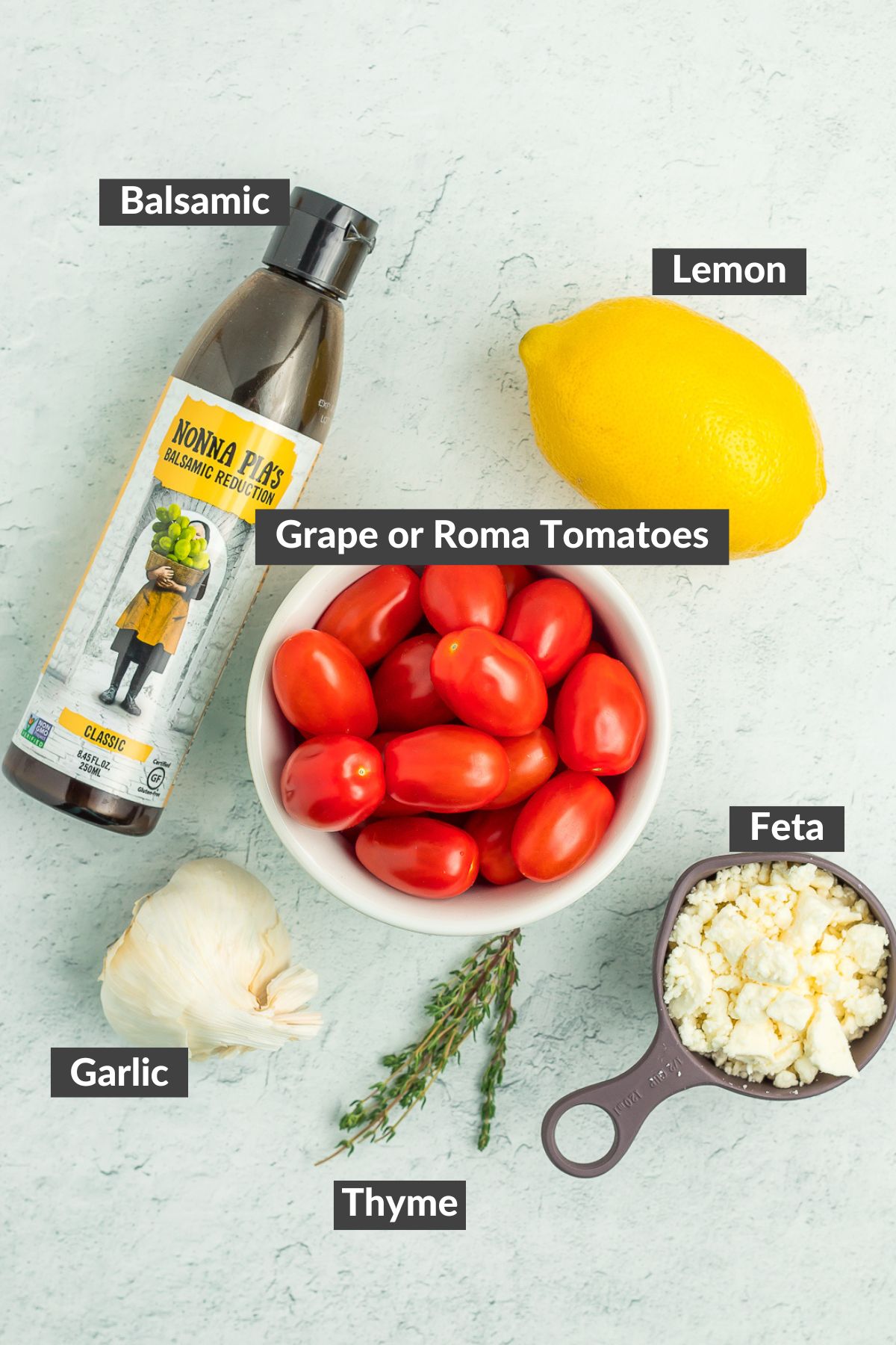 lemon, balsamic, cheese, garlic, thyme, and tomatoes on a white speckled board.