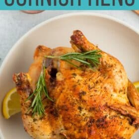 a roasted air fryer cornish hen on a white plate with sage, lemon, and a bowl of salt.